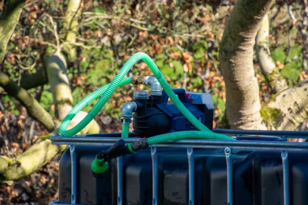 cuve-ibc-noir-avec-pompe-sur-batterie-1000L-renouvele-palette-acier-plastique-vue-de-cote-arrieere-avec-tuyau-sortant.webp